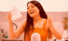 a woman in an orange tank top is laughing and holding a piece of paper in her hand