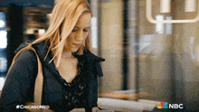 a woman is looking at her phone with a nbc logo in the corner
