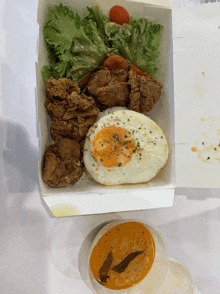 a box of food with fried chicken eggs and salad