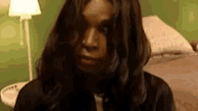 a woman with long dark hair is standing in front of a bed and a lamp .