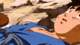 a man in a blue shirt is laying on a rocky ground .