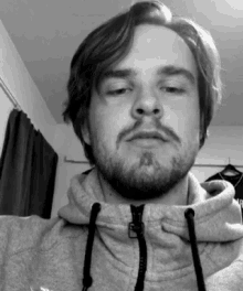a black and white photo of a man with a beard wearing a grey hoodie .