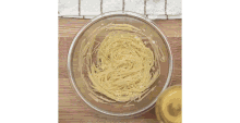 a glass bowl filled with noodles and a bottle of oil on a wooden table .