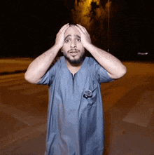a man in a blue shirt is holding his head with his hands