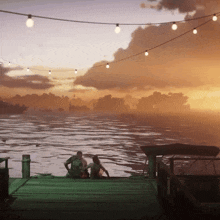 a couple sits on a dock looking out over the water at sunset