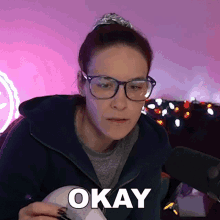 a woman wearing glasses and a hoodie says okay in front of a microphone