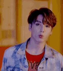 a young man wearing a denim jacket and a red shirt with the word love on it is making a funny face .
