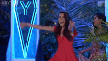a woman in a red dress is dancing in front of a neon sign that says y.