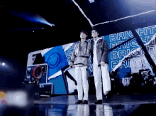 two men stand on a stage in front of a bright sign