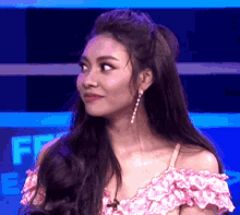 a woman wearing a pink off the shoulder top and earrings looks at the camera .