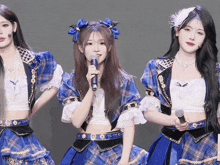 a girl in a blue plaid dress holds a microphone in her right hand