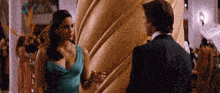 a woman in a blue dress is holding a glass of wine and talking to a man in a suit