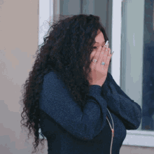 a woman with curly hair and a ring on her finger covering her face
