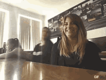 a woman sits at a table with a gif me logo on the bottom right