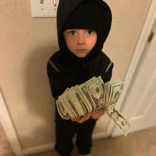 a young boy in a hooded jacket holds a stack of 20 dollar bills