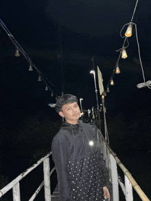 a young man in a black jacket stands on a dock at night