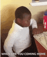 a little boy is sitting at a table and looking at something with the words " when are you coming home " below him