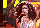 a woman singing into a microphone with a necklace around her neck