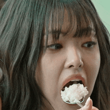 a young woman is eating rice with a spoon in her mouth