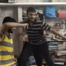 two men are dancing in a room with a lot of books on the shelf .