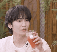 a young man is holding a glass of red liquid in his hand