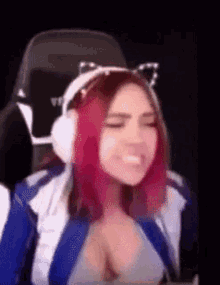 a woman with pink hair and cat ears is wearing headphones and sitting in a chair .
