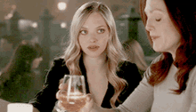 two women are sitting at a table one is holding a wine glass