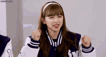 a girl wearing a baseball jacket and a headband is making a fist gesture .