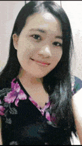 a woman with long black hair is smiling and wearing a floral top