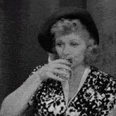 a woman in a black hat drinks from a glass in front of a wall that has the word pa on it