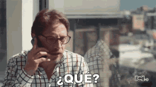 a man with glasses is talking on a cell phone and says " qué "