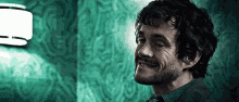 a man with curly hair and a beard is smiling in a room with a green wall .