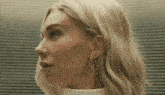 a close up of a woman 's face with blonde hair and a white turtleneck .