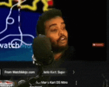 a man wearing headphones is talking into a microphone in front of a screen that says watch