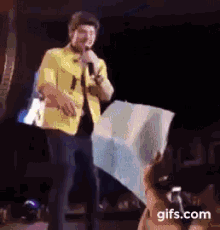 a man in a yellow jacket is standing on a stage with a microphone and holding a flag .
