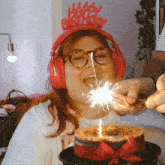 a woman wearing headphones and a happy birthday headband lighting a birthday cake