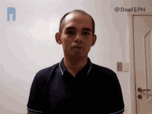 a man in a blue shirt stands in front of a white wall with the hashtag @deafeph on the bottom