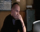 a man is sitting in front of a computer screen and covering his mouth with his hand