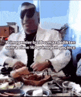 a man in a suit and sunglasses is sitting at a table with a plate of food