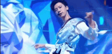 a man in a blue kimono is dancing on a stage in front of a blue background .