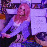 a girl with pink hair is sitting on a bed next to a sign that says i hate myself