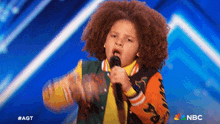 a young boy singing into a microphone with a nbc logo behind him