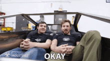 two men sitting in a car with the word okay on the bottom right