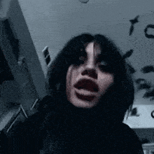 a woman with black hair is making a funny face in a dark room with birds on the ceiling .