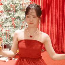 a woman in a red dress with a pearl necklace stands in front of a christmas tree