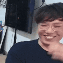 a young man wearing glasses and a blue shirt is smiling while standing in front of a television .