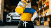 a dog in a yellow and blue shirt is holding a bottle of orange juice in a garage .