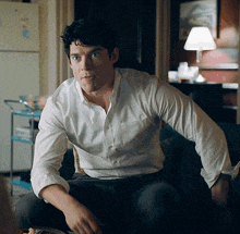 a man in a white shirt is sitting on a couch in front of a refrigerator