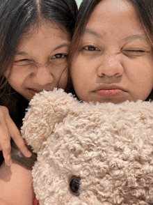 two girls are making funny faces with a teddy bear