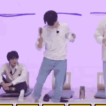 a man is dancing in front of a purple wall while another man sits on the floor .
